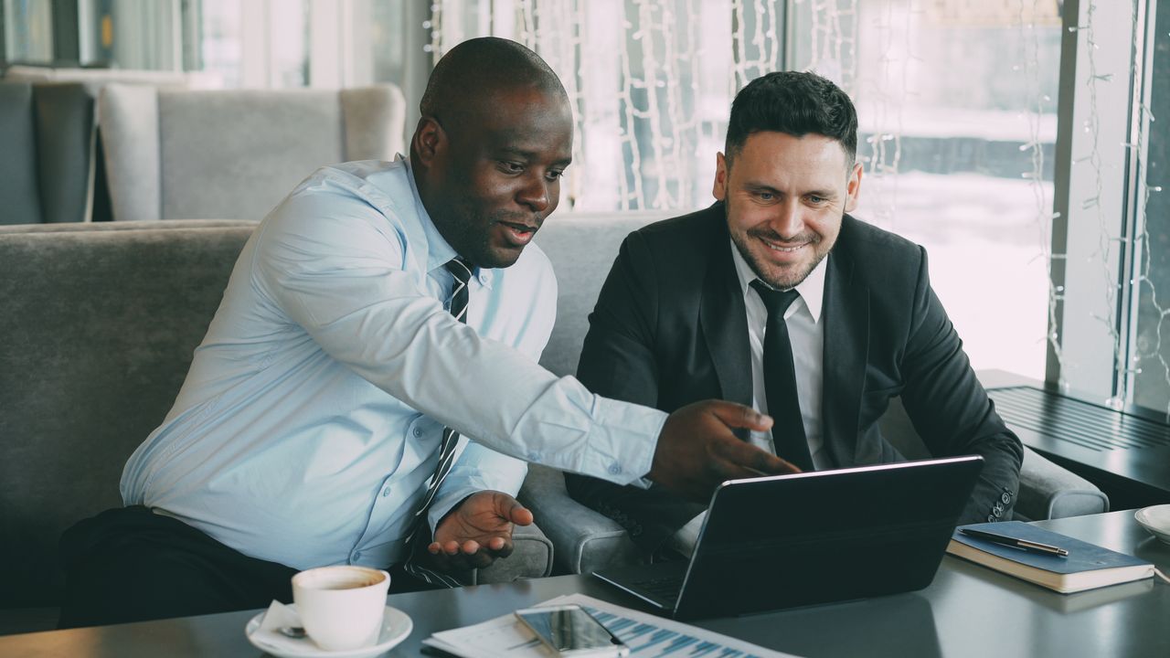 Mastering the First Impression: Your intriguing post title goes here Two businessmen discussing work while using a laptop in a cafe setting.